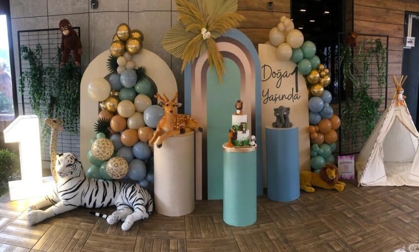 Safari konseptli bir çocuk doğum günü organizasyonunda, yeşil ve kahverengi tonlarda balon süslemeleri, hayvan figürleri ve temaya uygun masa dekorasyonu, eğlenceli bir atmosfer yaratıyor.