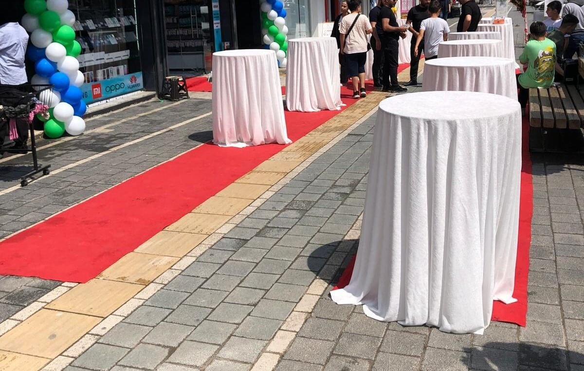 Açılış öncesi hazırlıklar sırasında rengarenk balon süsleme kemerinin kurulduğu, etrafı insanlarla dolu canlı bir mağaza önü sahnesi.