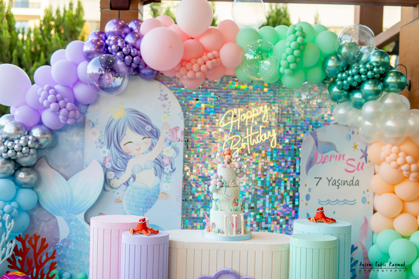 Palyaço kostümlü animatörün, yüz boyama etkinliği sırasında bir çocuğun yanağına kelebek deseni çizerken, diğer çocukların merakla izlediği an.